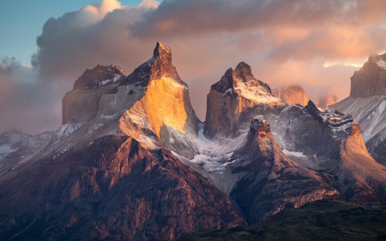 a mountain range covered in snow under a cloudy sky